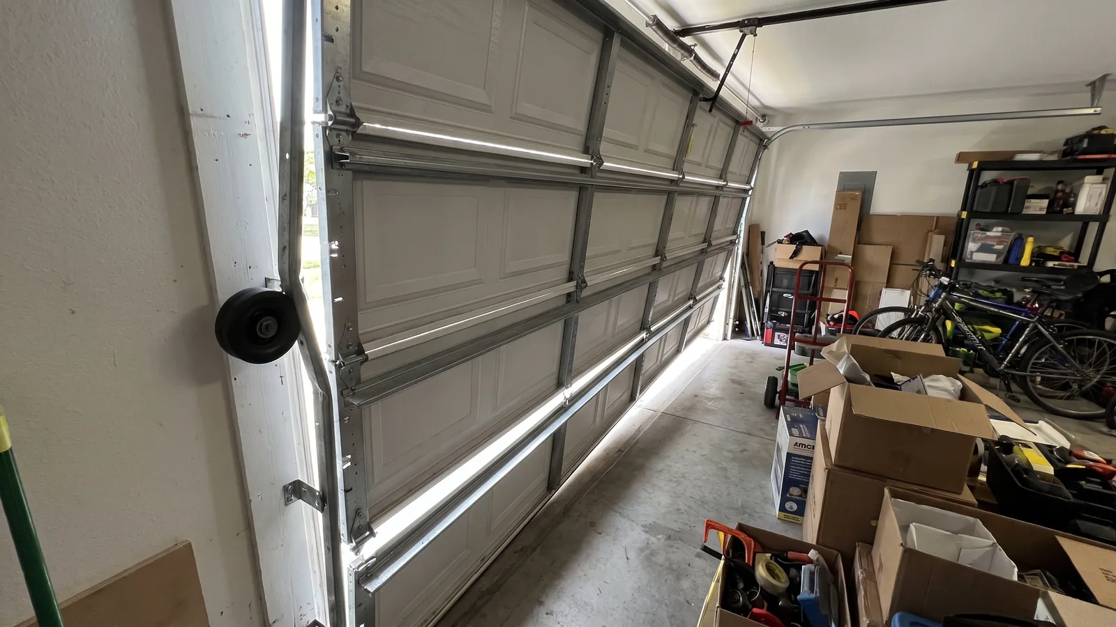 Sectional garage door hanging crooked and jammed where the rail is bent, one roller out of the track, seen from inside a Midwest garage